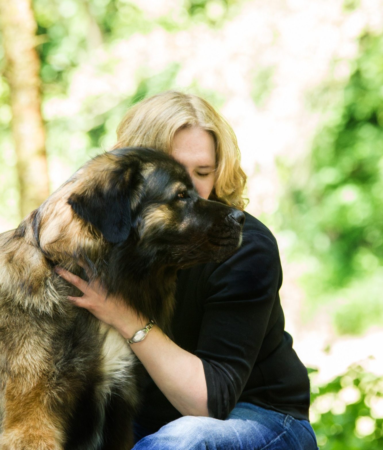 Frau umarmt großen Hund in einer grünen, blühenden Umgebung.