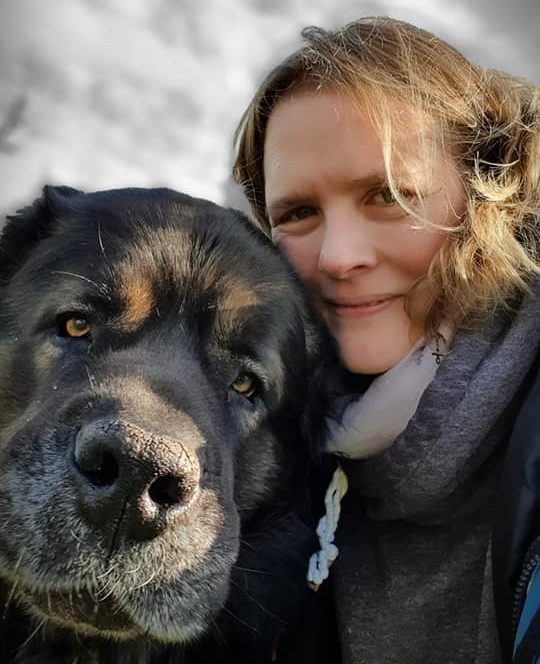 Frau mit lockigem Haar posiert lächelnd neben einem großen, freundlichen Hund.